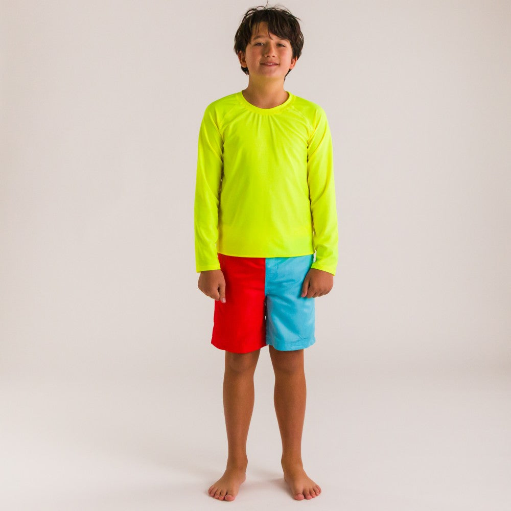 Child wearing a bright yellow long-sleeve rash top and colorful shorts on a plain background