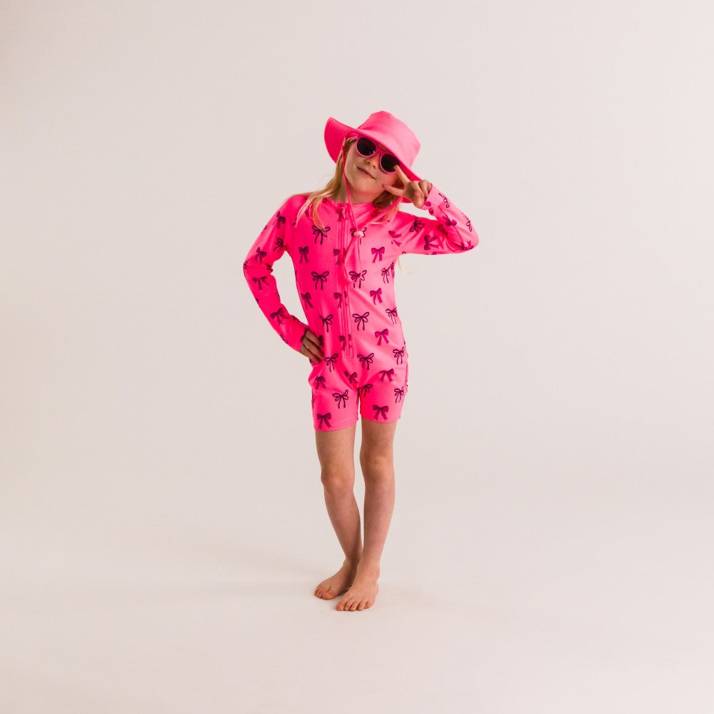 Child wearing a bright pink UV protective swim suit with black bows on a plain background