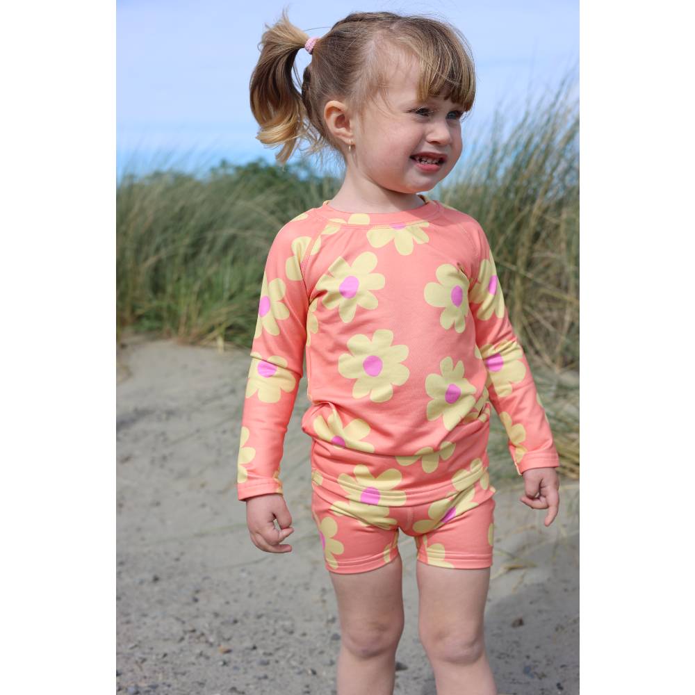 Child wearing a pink floral rash top and shorts on a beach