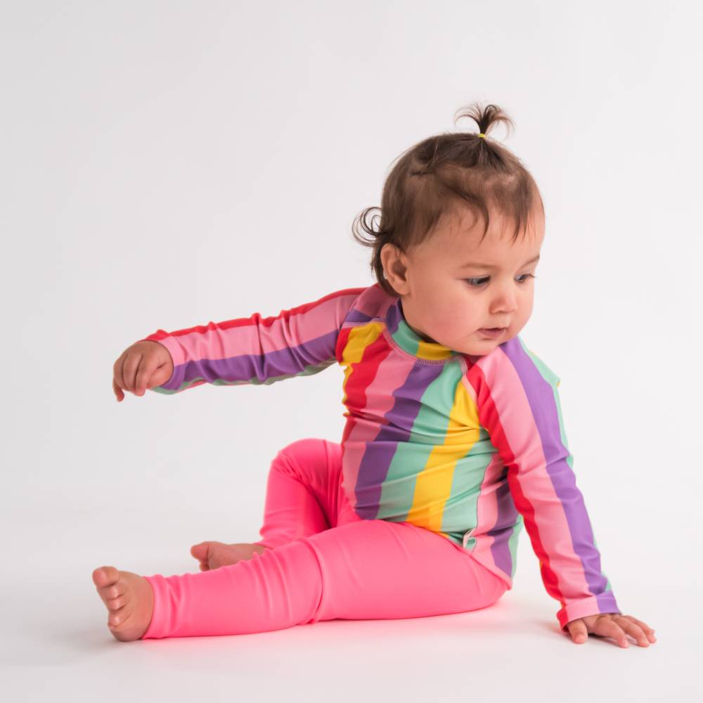 Child wearing a colorful striped rash vest and pink neon swim leggings on a white background
