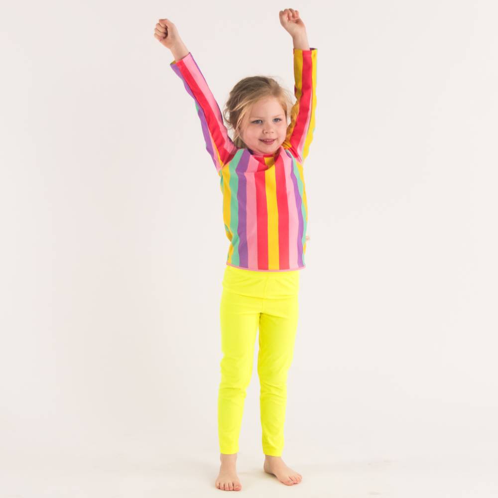 Child wearing a colorful striped swim rash vest and neon yellow swim leggings on a white background