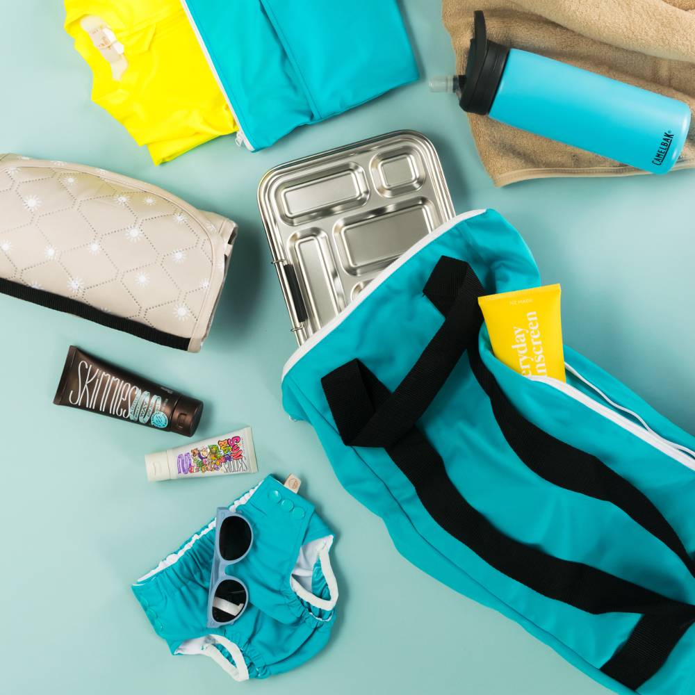 Collection of swim and lunch items including a blue swim bag, sunglasses, and toiletries on a light blue background