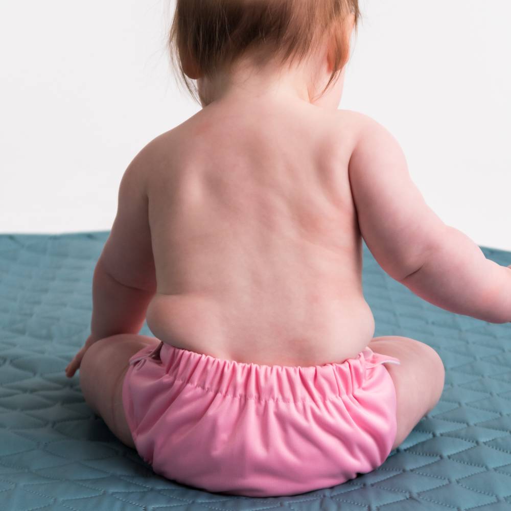 Baby wearing a pink swim nappy sitting on a textured blue surface.