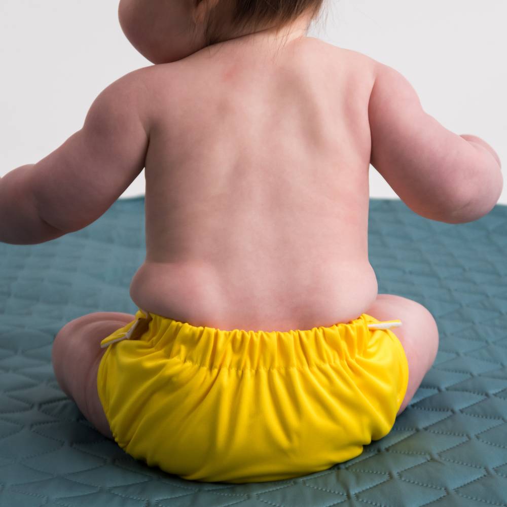Toddler wearing a Nestling reusable swim nappy sitting on a playmat