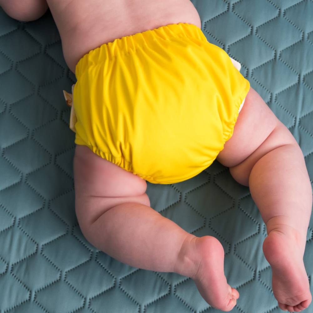 Baby wearing a yellow reusable nestling swim nappy on a textured blue surface