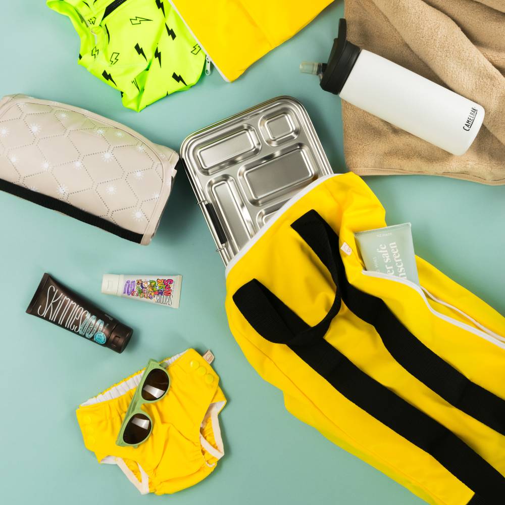 Collection of yellow and black swim items, a metal lunch box, and accessories on a light blue background.