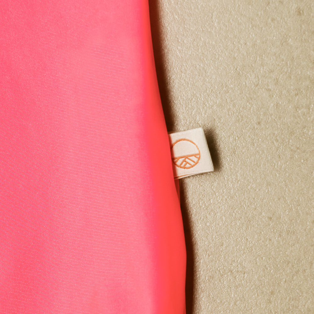 Close-up of a pink swim fabric with a beige label featuring a Nestling brand logo on a textured beige background.