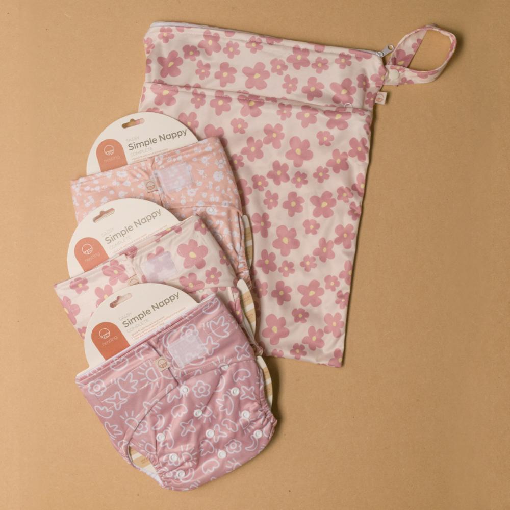 Set of pink floral-patterned baby products including a wet bag,3 cloth nappies on a brown background.