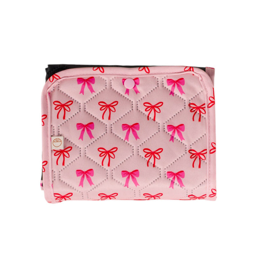Pink quilted travel change mat with red and pink bow patterns on a white background