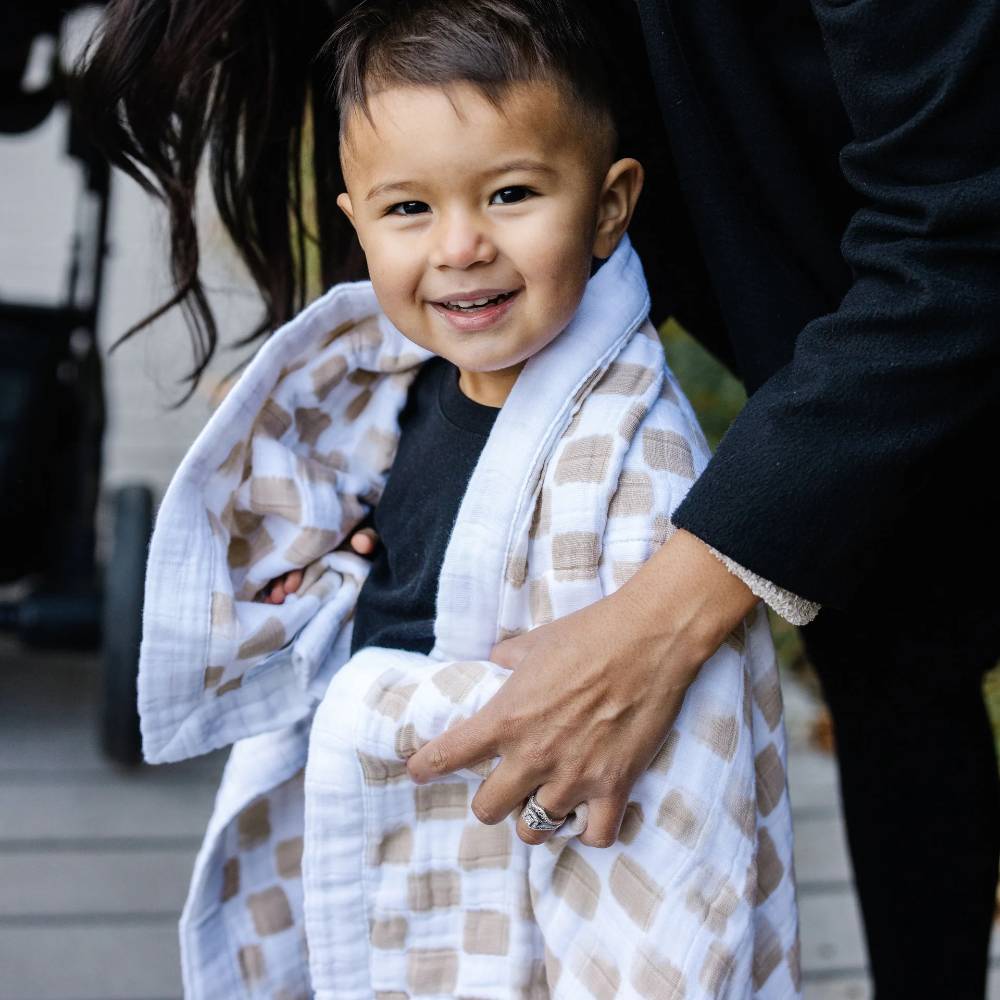 Child wrapped in a beige and white checkered blanket with a blurred background
