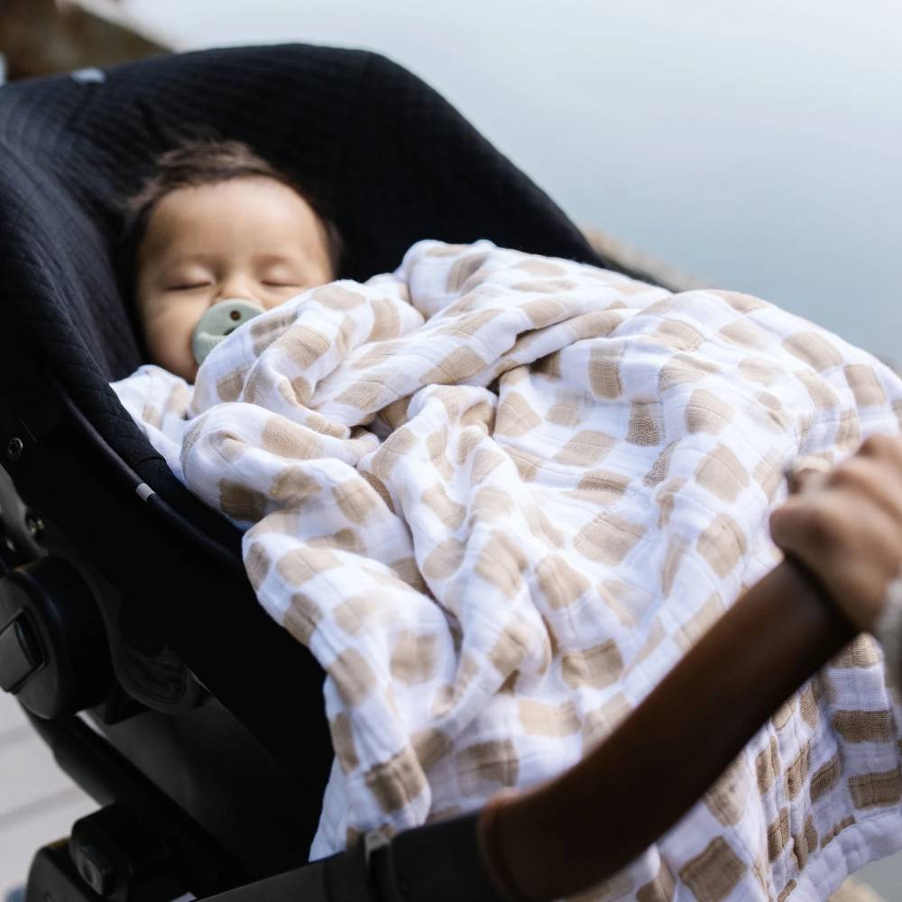 Baby sleeping in a stroller with a beige and white checkered blanket