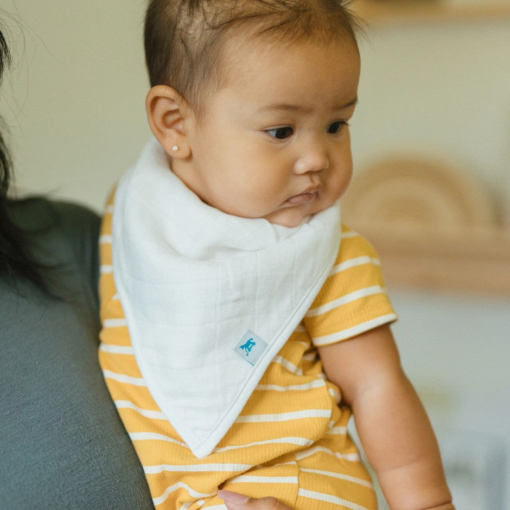 Baby wearing a yellow and white striped outfit with a white muslin bandana bib, sitting on a couch.