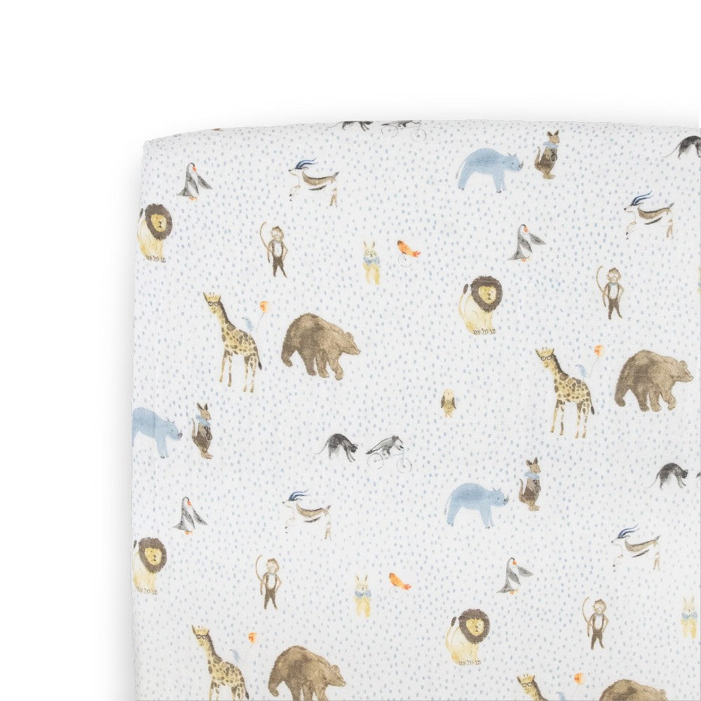A white cotton muslin fitted sheet with blue dots and animal pattern on a bed with a white background