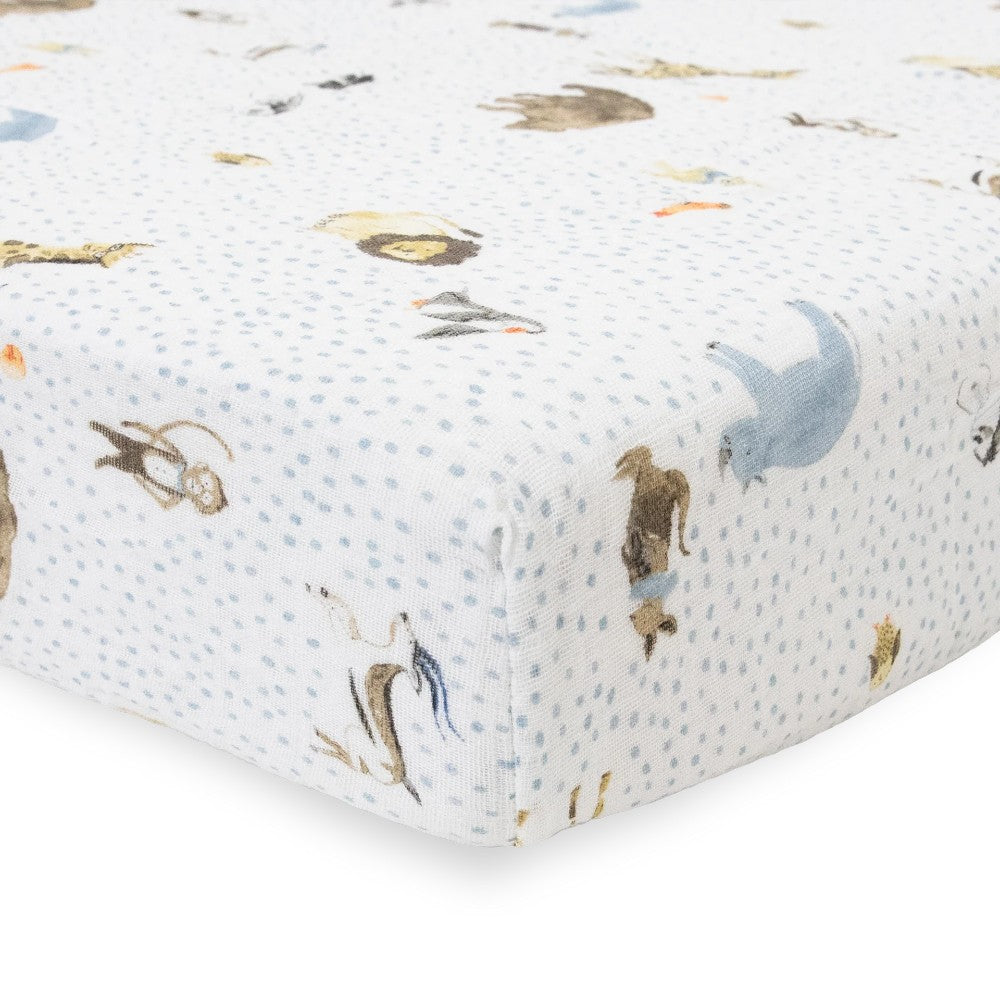Close-up of white cotton muslin fitted sheet with blue dots and animal pattern on a bed with a white background