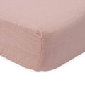 Close-up of cotton muslin pink fitted sheet on a bed with a white background