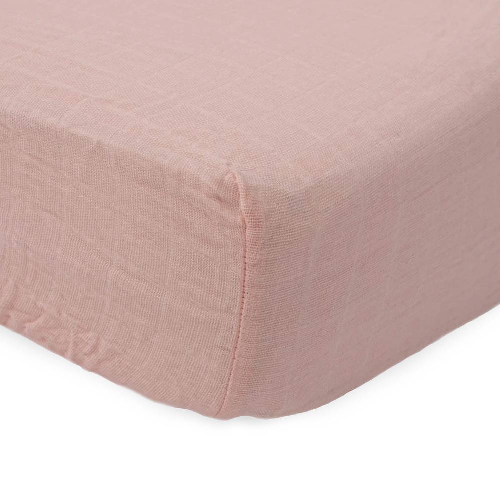 Close-up of cotton muslin pink fitted sheet on a bed with a white background