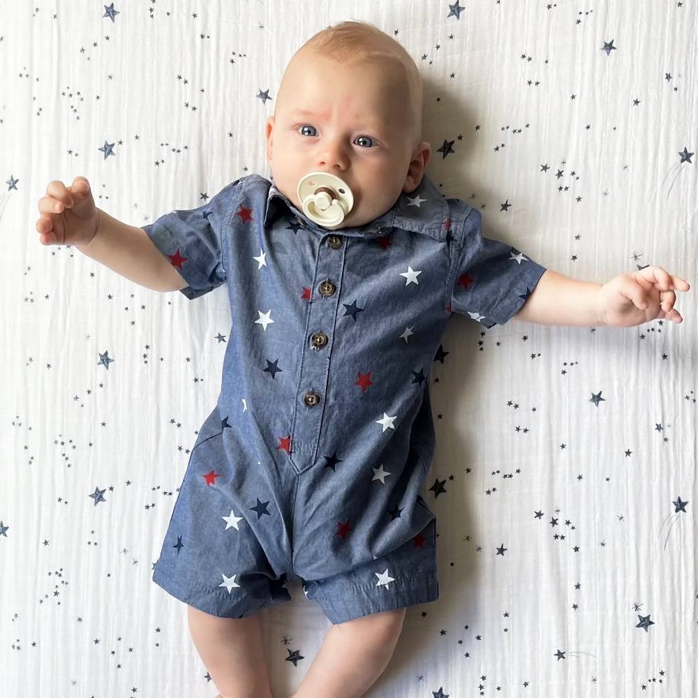 Baby wearing a blue romper with star patterns laying on a white sheet with navy blue star pattern 