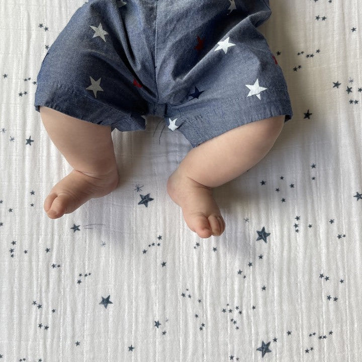 Baby legs in blue pants with star pattern on a star-patterned cotton muslin sheet