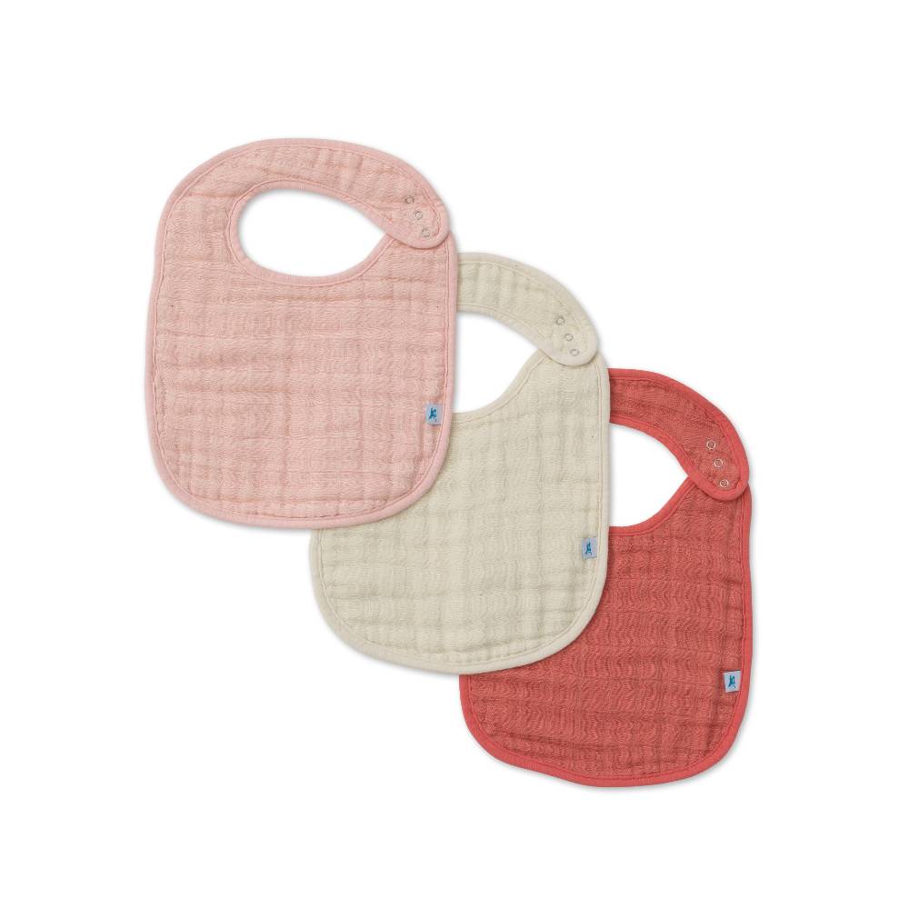 Set of three cotton muslin baby bibs with light pink, cream/beige and rose pink on a white background