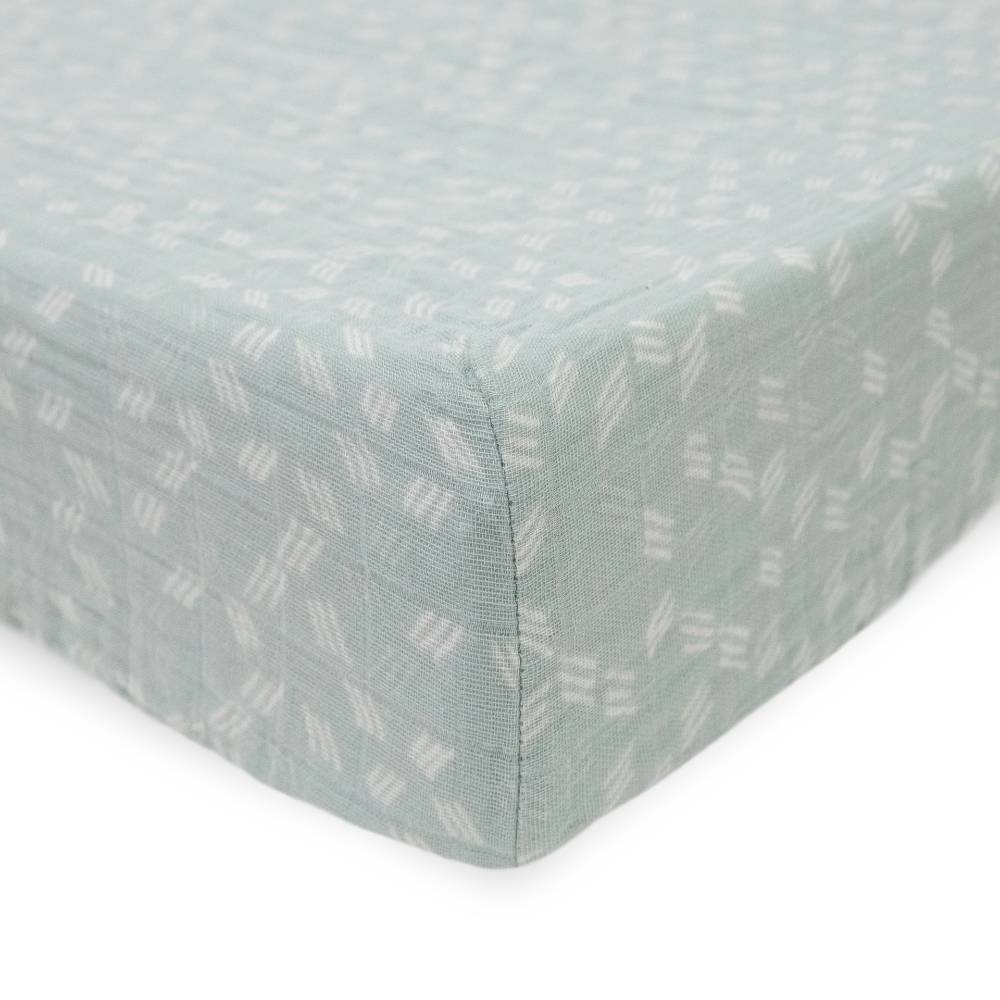 Little unicorn cotton muslin changing pad cover in a light green/blue with white pattern on a bed with white background