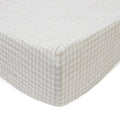 Little unicorn cotton muslin changing pad cover in a tan gingham pattern on a bed with white background