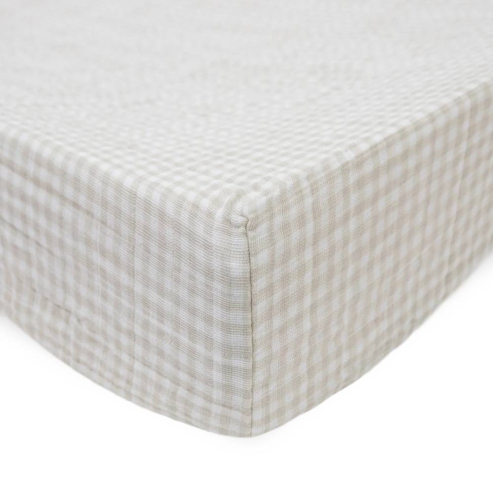 Little unicorn cotton muslin changing pad cover in a tan gingham pattern on a bed with white background
