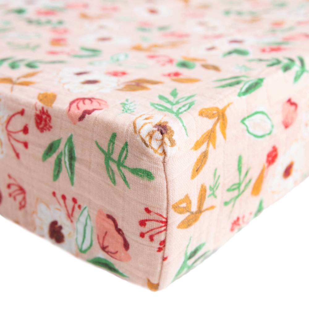 Little unicorn cotton muslin changing pad cover in a pink floral pattern on a bed with white background