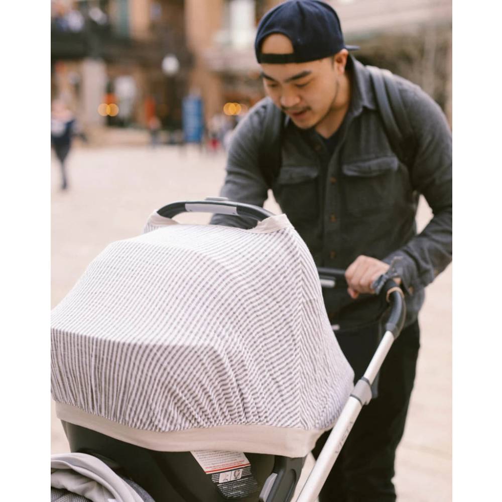 Man pushing a stroller with a little unicorn grey and white striped car seat canopy on a city street