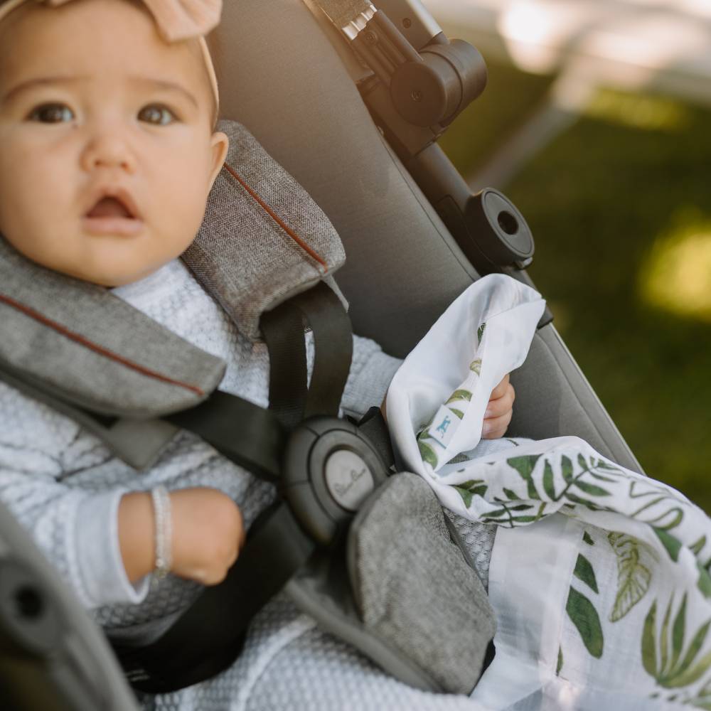 Baby in a stroller holding a green and white tropical leaf themed security blanket