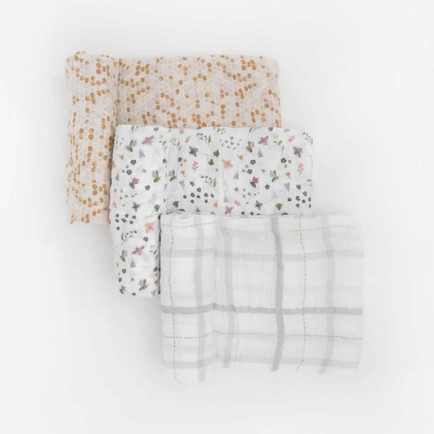 Three baby cotton muslin swaddle blankets with a honeycomb, garden theme and light plaid patterns on a white background