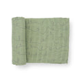 A green cotton muslin swaddle blanket with desert line patterns on a white background
