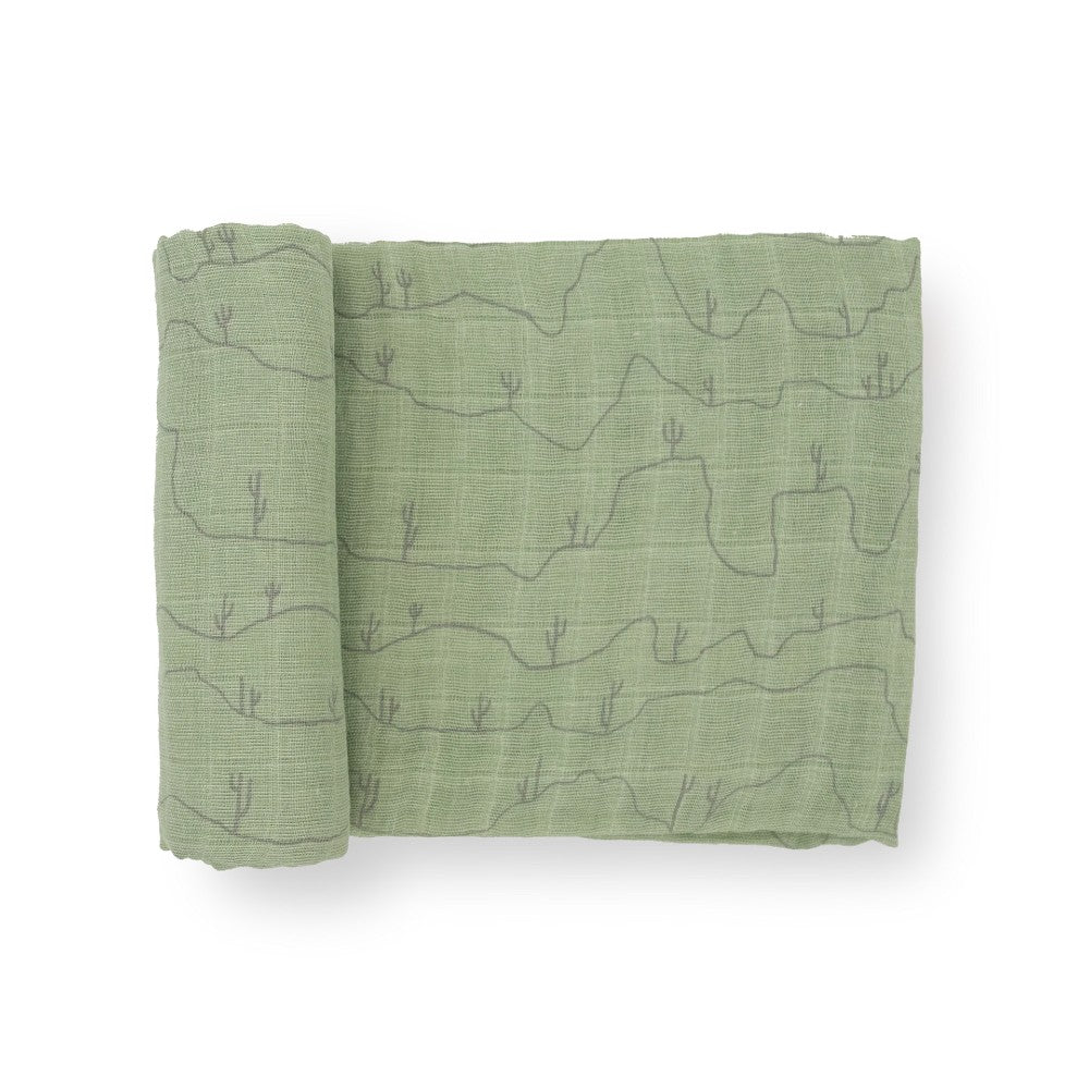 A green cotton muslin swaddle blanket with desert line patterns on a white background
