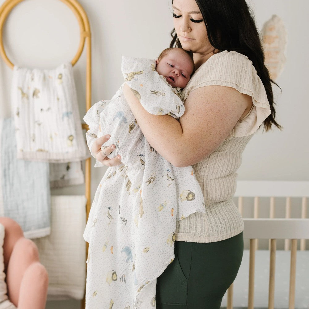 Woman holding a baby wrapped in a little unicorn muslin swaddle wrap with animal design in a nursery setting