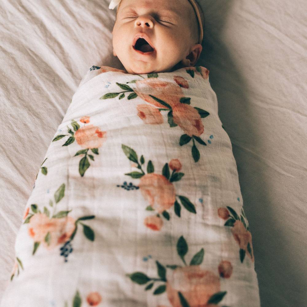 Newborn baby wrapped in a watercolour roses floral muslin swaddle blanket on a soft surface