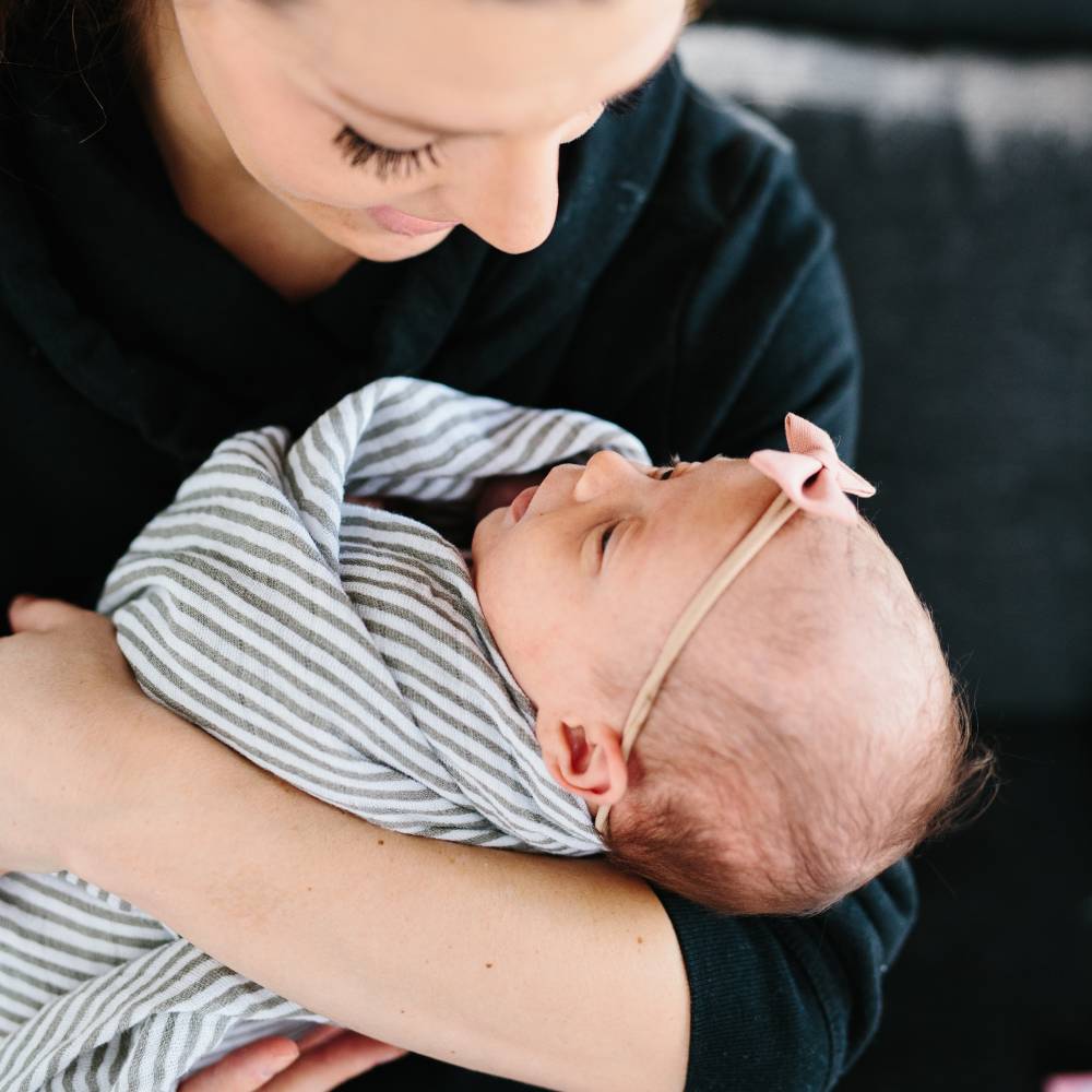 Woman holding a baby wrapped in a grey and white striped muslin swaddle blanket