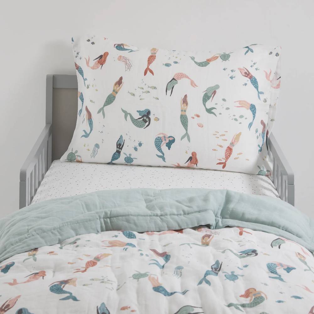 Children's mermaid-themed cotton muslin bedding set on a bed with a light grey headboard and dotted sheet.