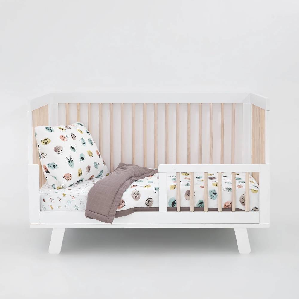 White and wooden crib with animal patterned white cotton muslin bedding on a white background