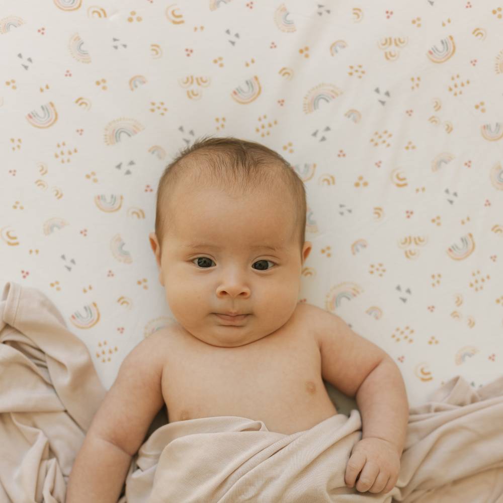 Baby lying on a rainbow patterned sheet with beige blanket with a neutral color palette