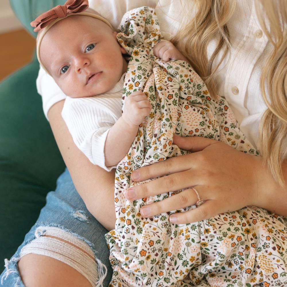 Baby in a white rib shirt being held by an adult with a floral stretch knit over top 