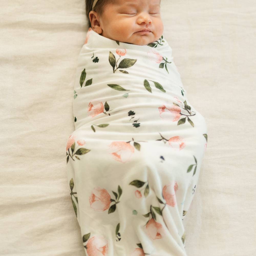 Newborn baby wrapped in a floral swaddle on a soft beige background