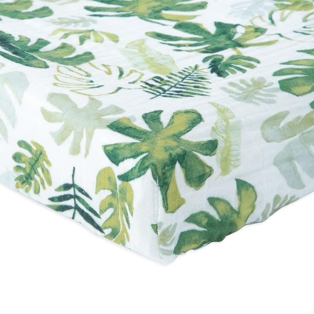 Little unicorn cotton muslin changing pad cover in a white and green tropical leaf pattern on a bed with white background