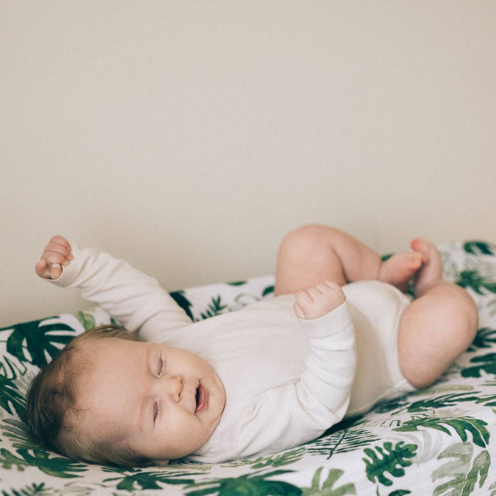 Baby lying on a green leaf-patterned cotton muslin changing pad cover against a plain background