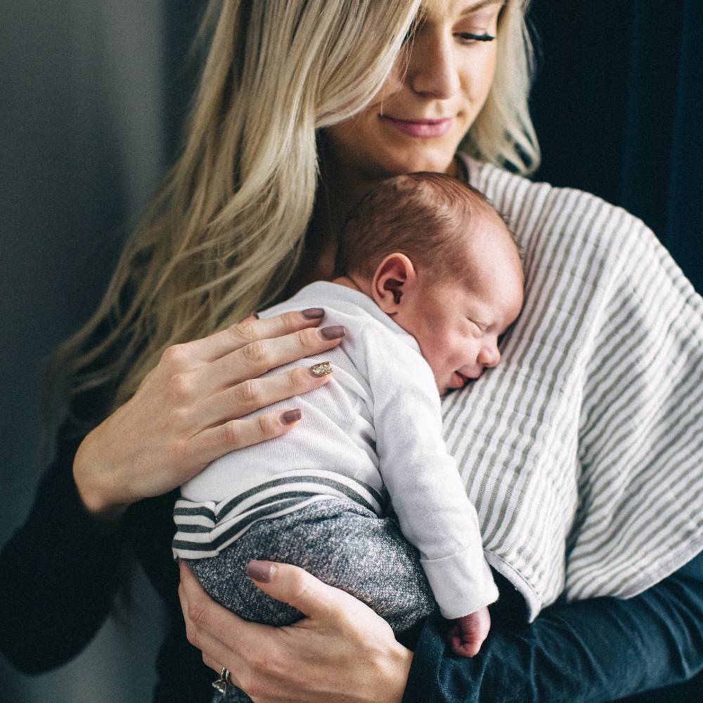 Woman holding a newborn baby with. Grey and white burp cloth against a dark background