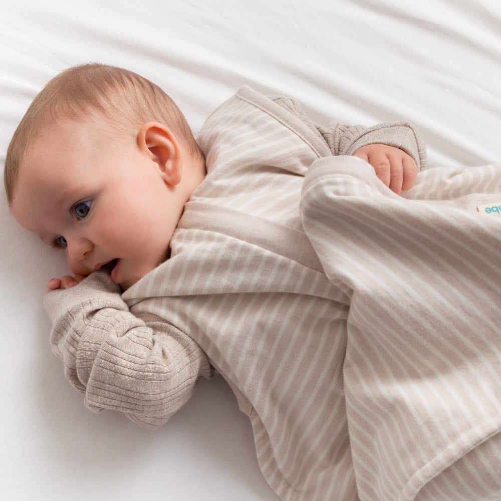 Baby lying on a white surface with a striped blanket