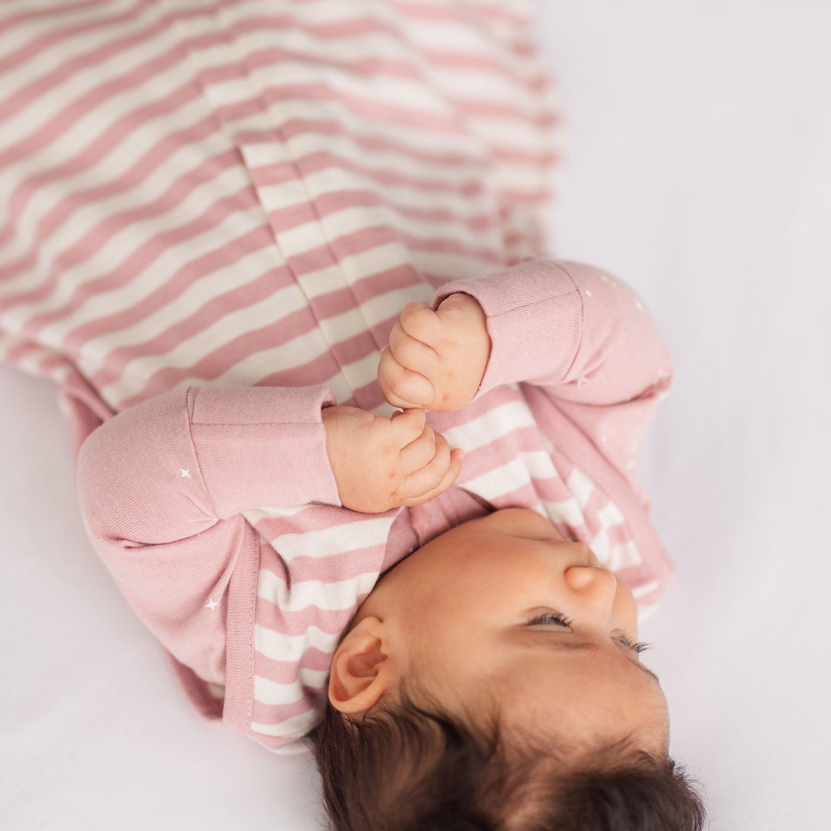 Baby wearing a pink and white striped outfit lying on a light surface
