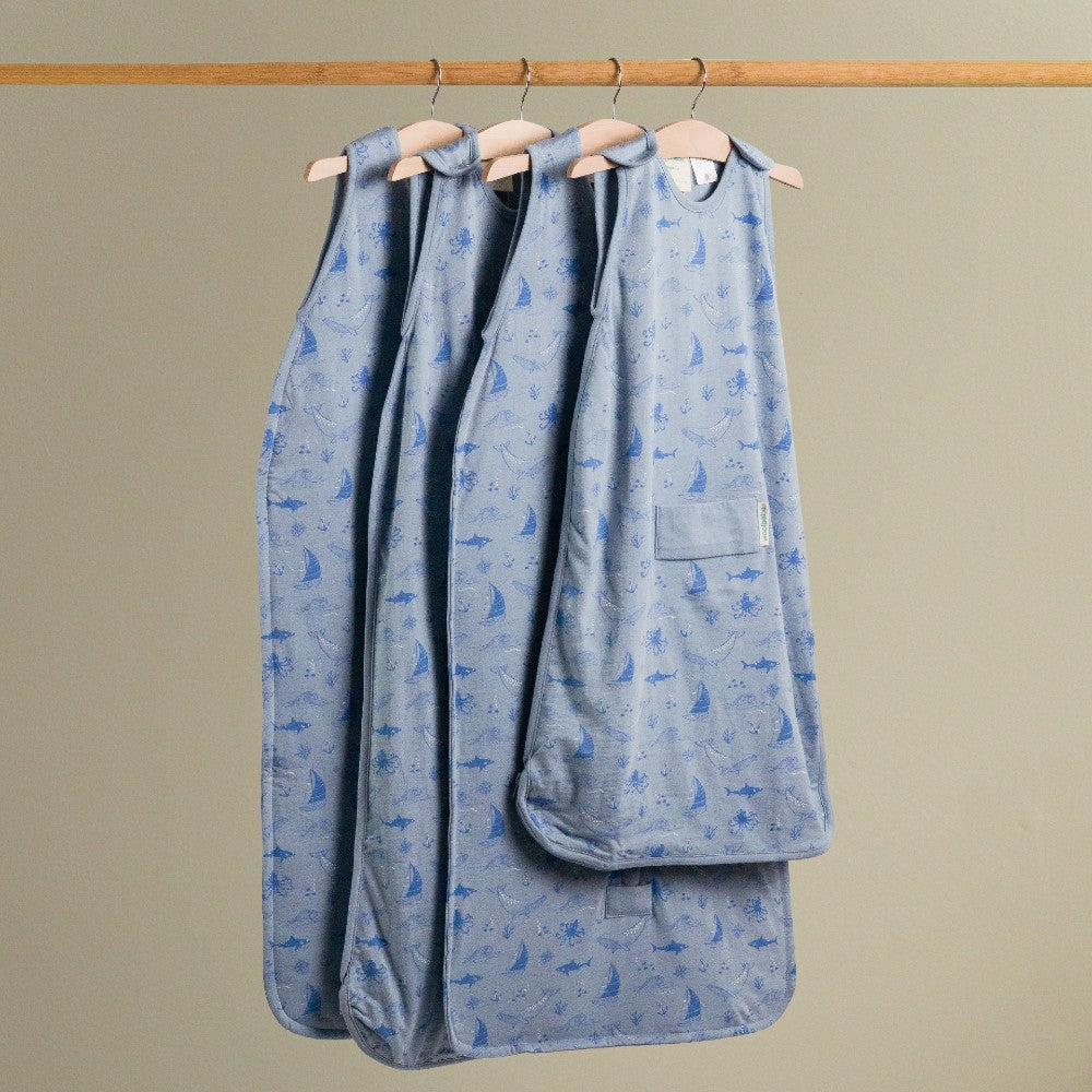 Blue Sail Away print woolbabe baby sleeping bag with whale pattern on hangers against a beige background