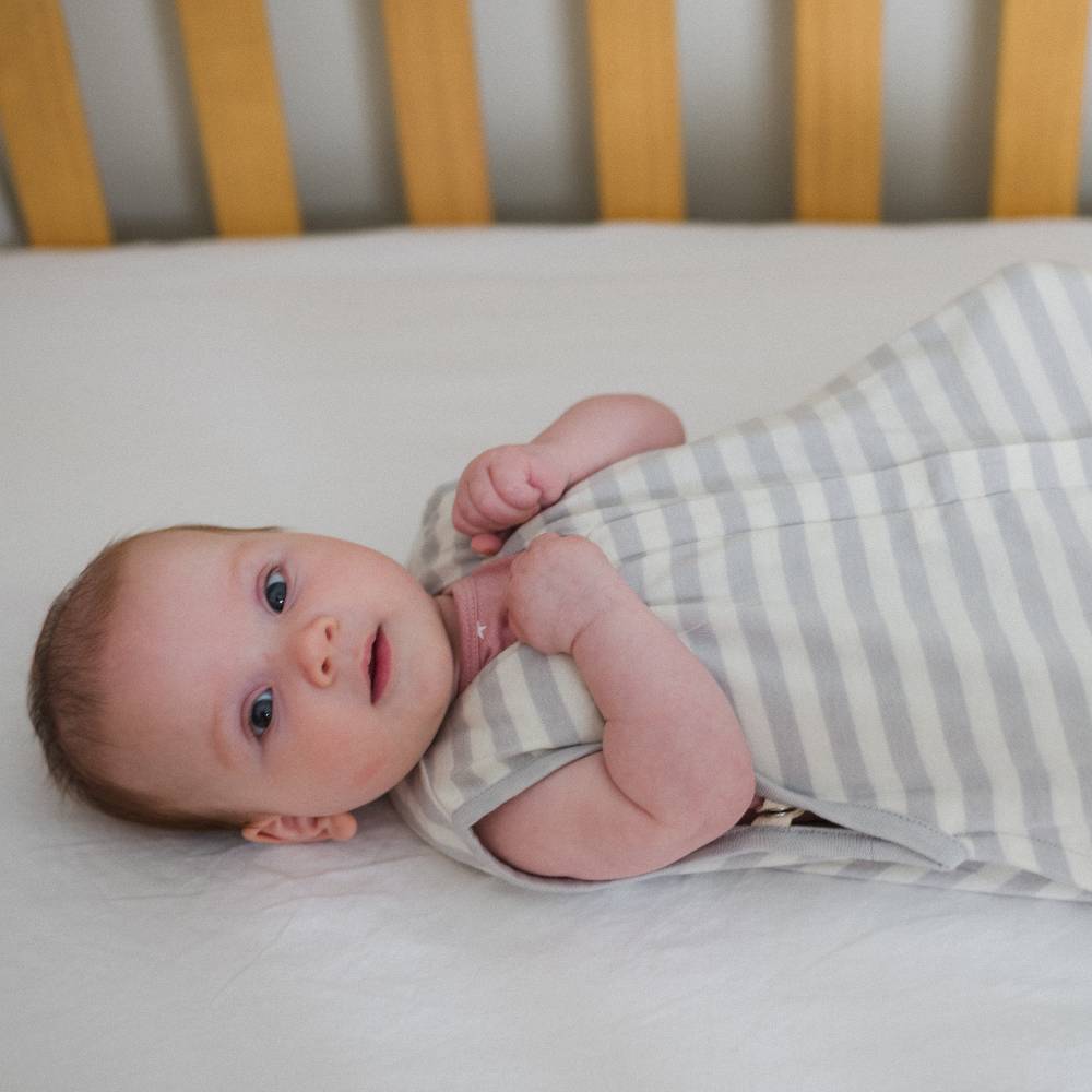 Newborn baby wrapped in a striped sleeping bag lying on a crib.
