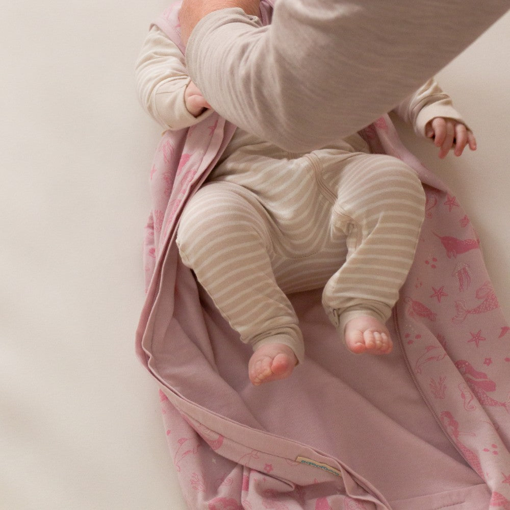Baby in striped outfit lying on a pink sleep sack with star pattern