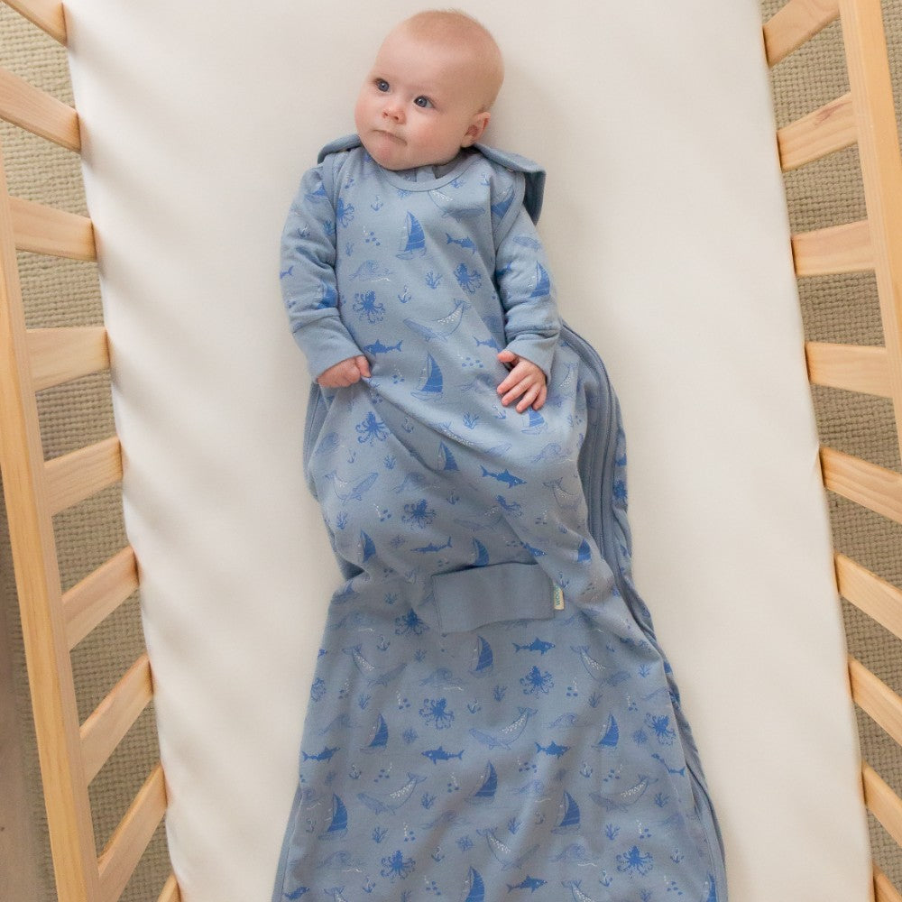 Baby wrapped in a blue patterned sleep sack with whale print in a crib.