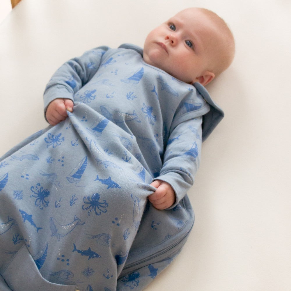 Baby wrapped in a blue woolbabe with sea creature patterns on a white background